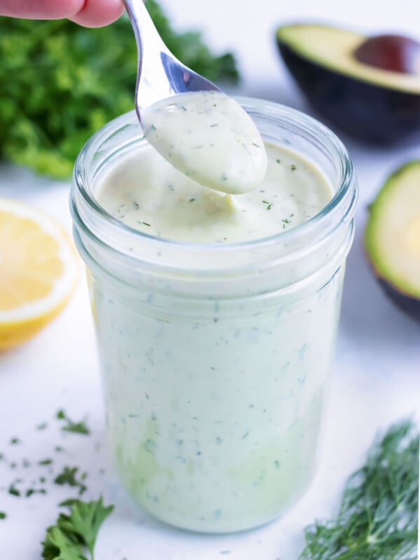 A spoon is used to lift avocado dressing from a mason jar.