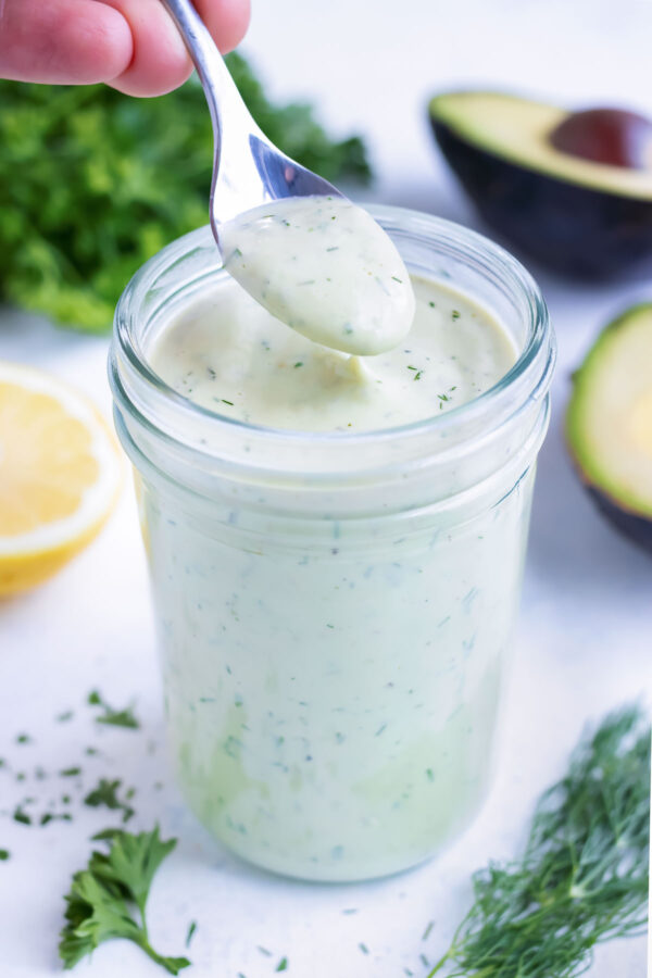 A spoon is used to lift avocado dressing from a mason jar.