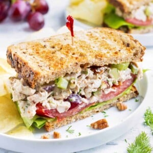 Chicken salad sandwich with a red toothpick on a white plate with potato chips.