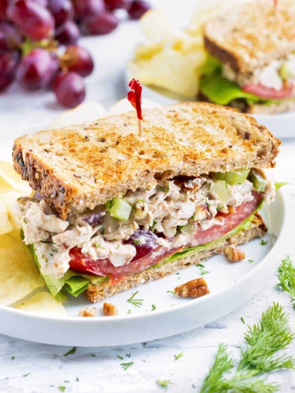 Chicken salad sandwich with a red toothpick on a white plate with potato chips.