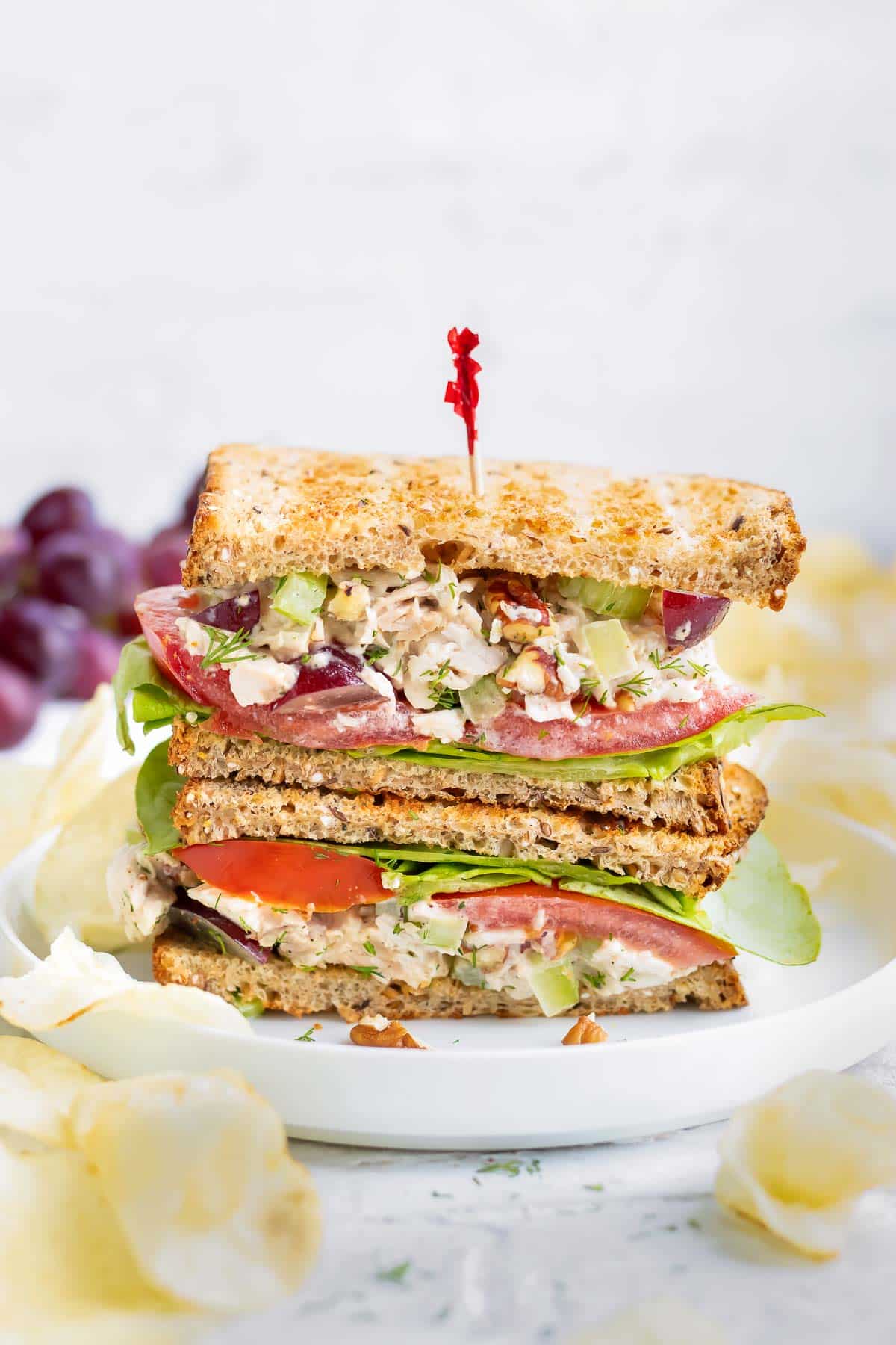 Healthy chicken salad recipe on toasted white bread in a stack on a white plate.
