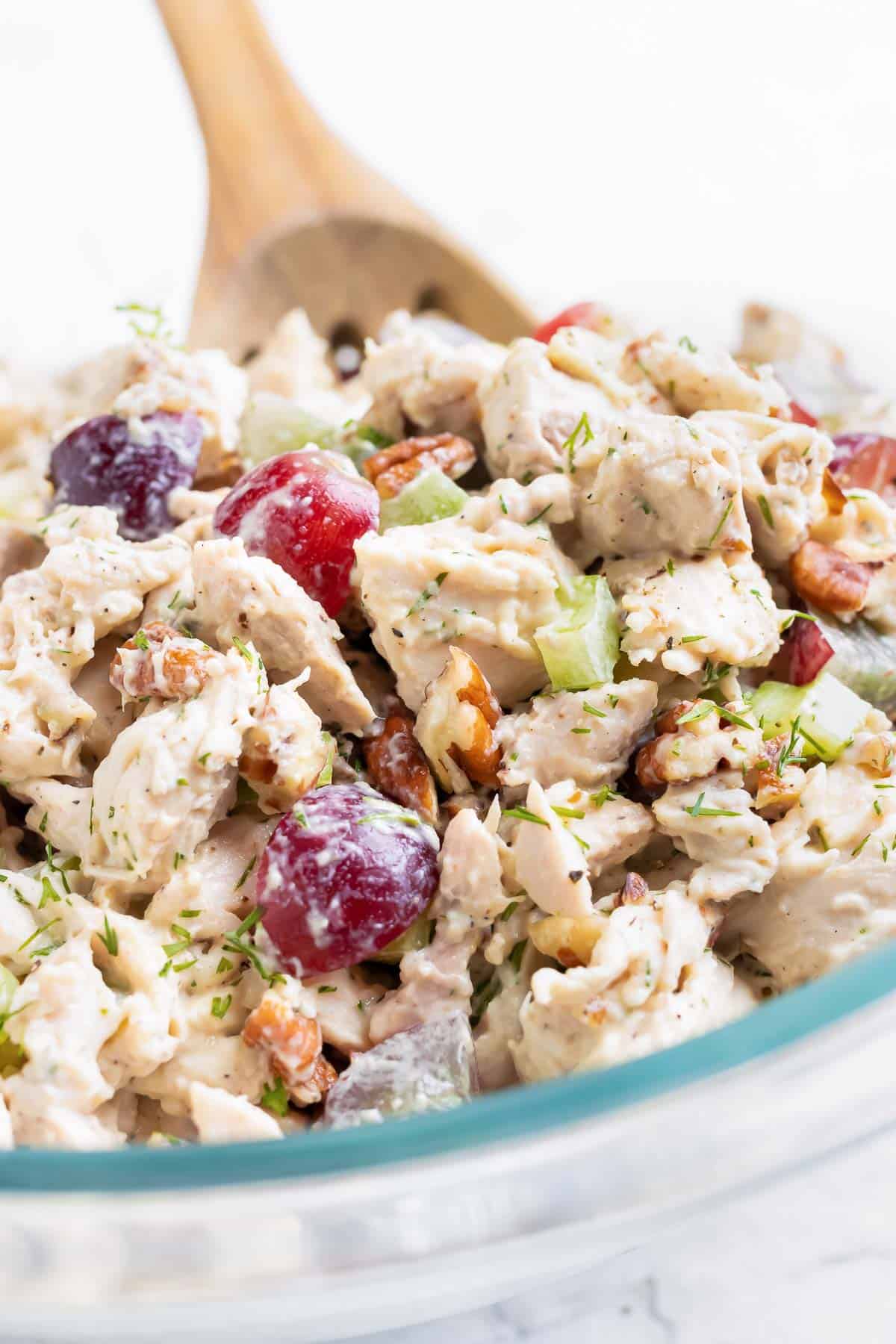 Healthy chicken salad with grapes in a clear glass bowl with a wooden spoon.