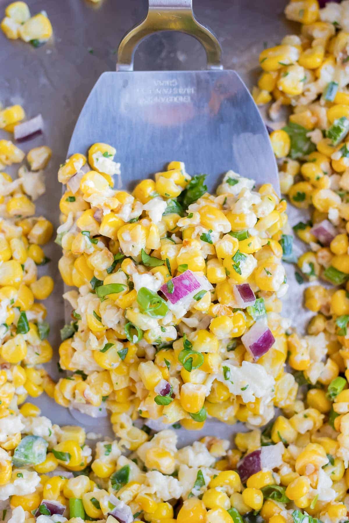 A stainless steel spatula scooping up a serving of a corn salad recipe as a side dish.