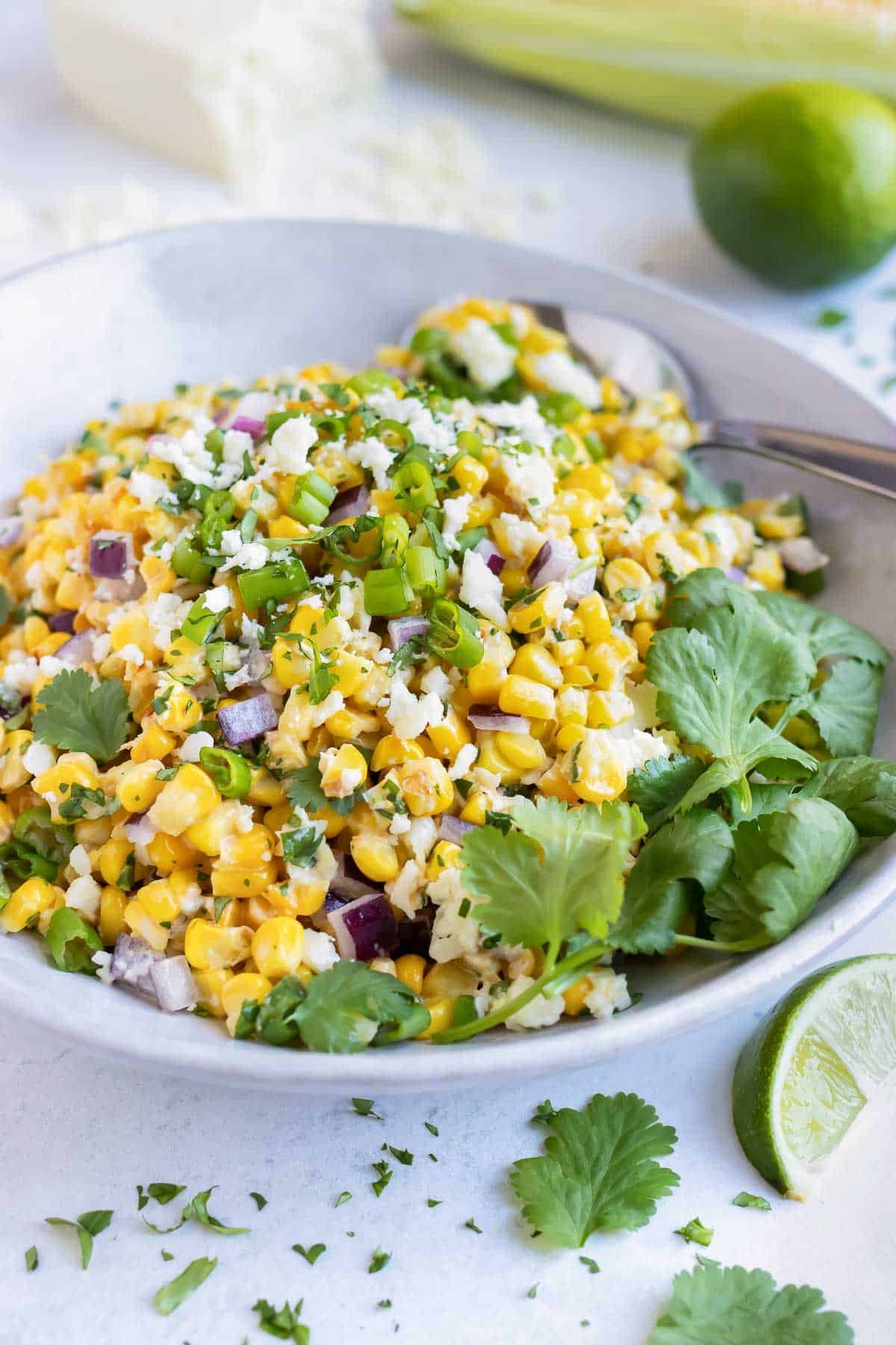Mexican street corn salad with cilantro and limes in a white serving bowl.