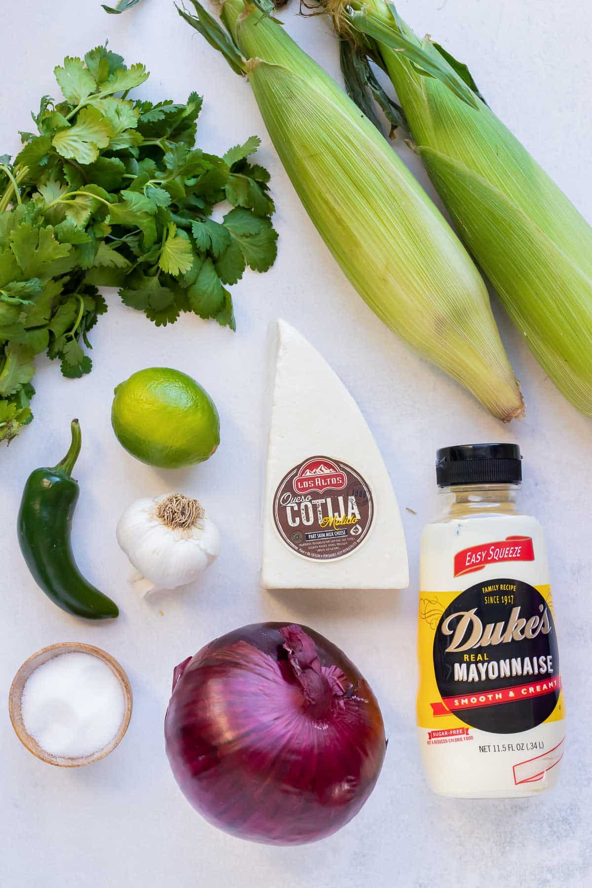 Fresh corn on the cob, cilantro, lime, jalapeno, mayonnaise, red onion, and cotija cheese as ingredients for a street corn salad.