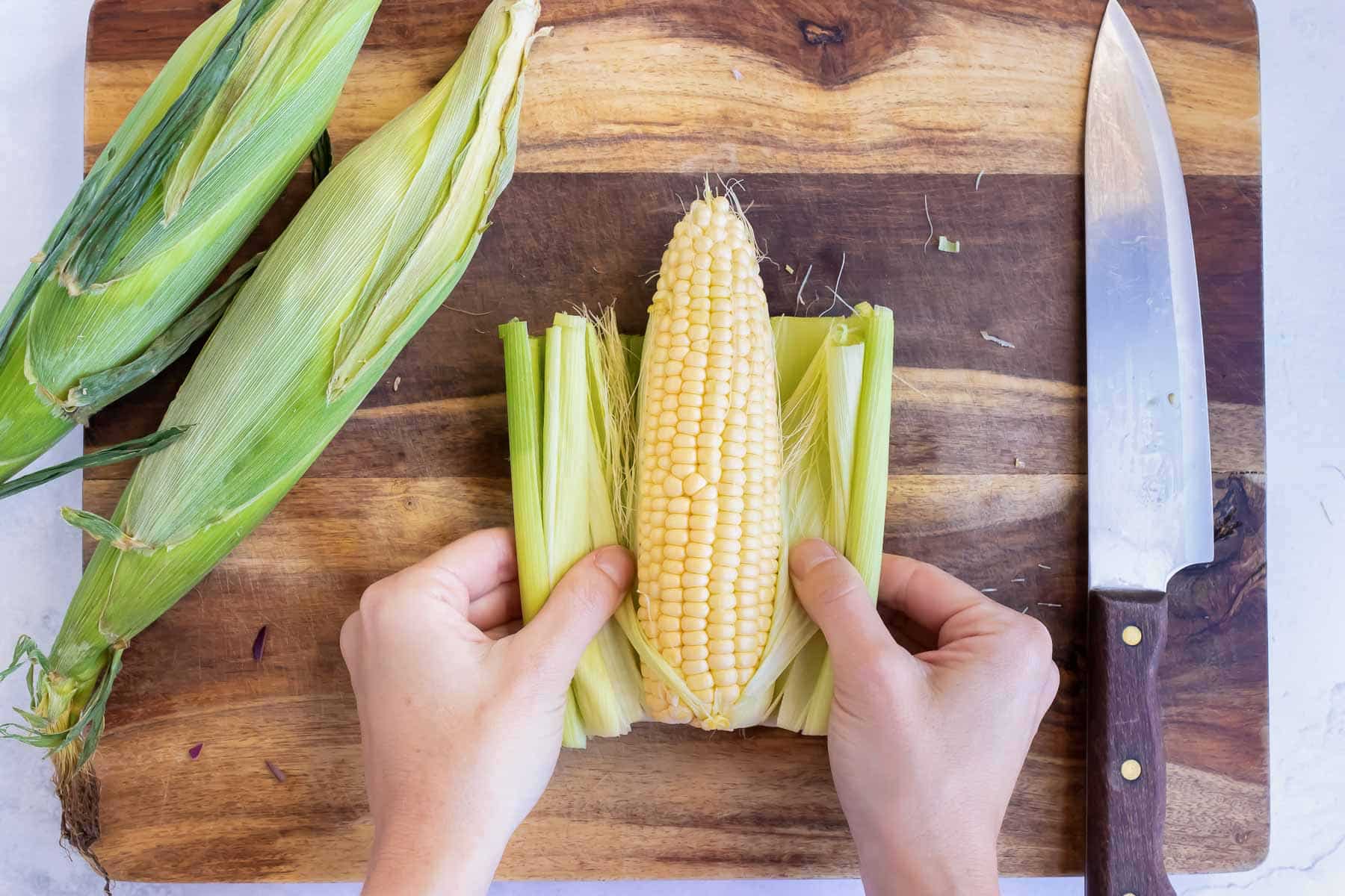 Hands pull the husks off of corn.