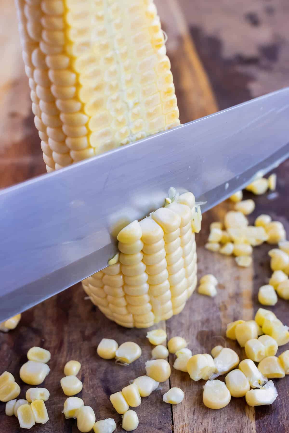 A knife slices corn kernels off the cob.