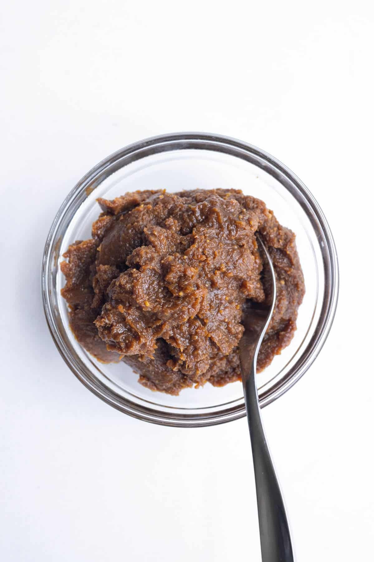 A glass bowl of red miso paste with a spoon dipped inside.