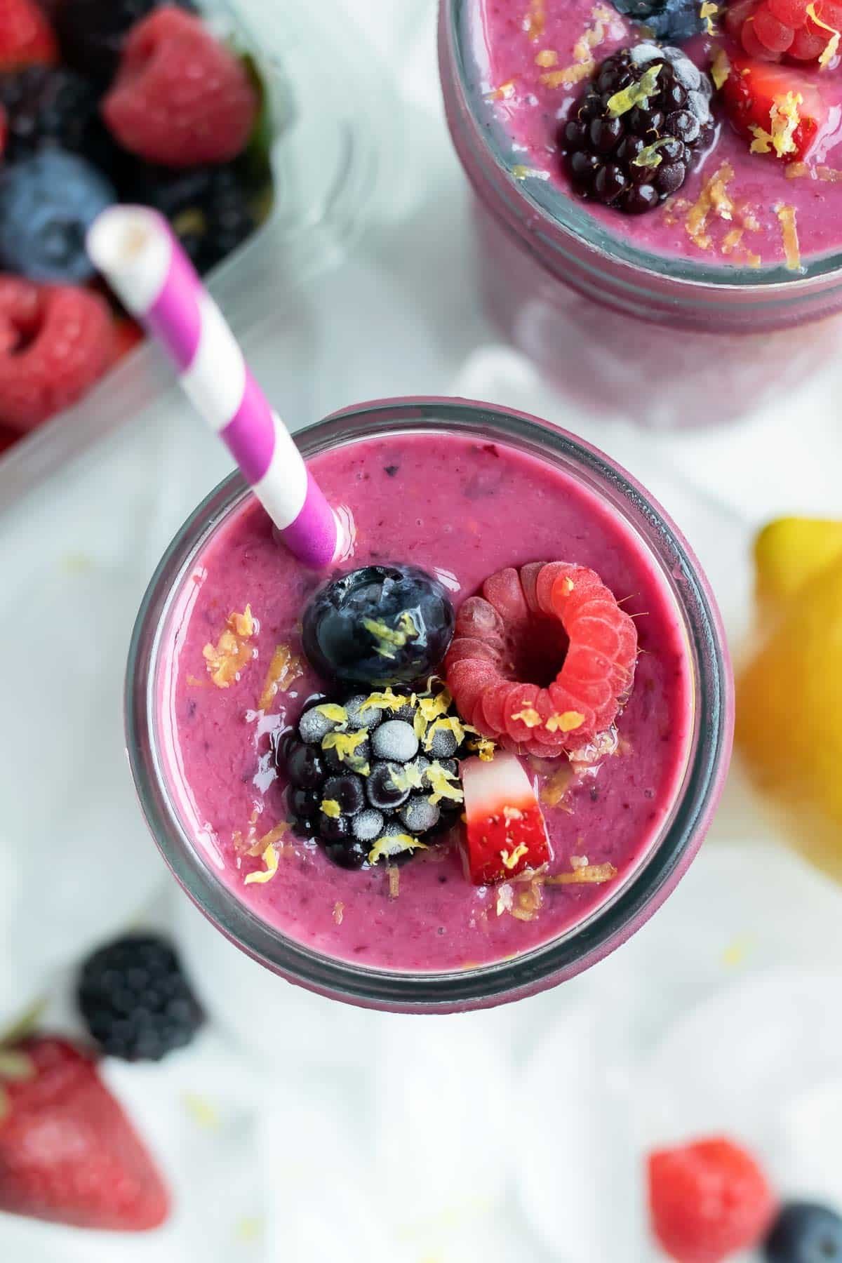 A berry smoothie is topped with frozen berries and fresh lemon zest.