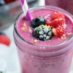 Mixed berry smoothies are topped with berries and drank with a straw.