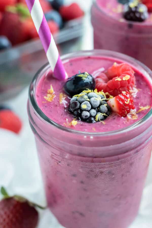 Mixed berry smoothies are topped with berries and drank with a straw.