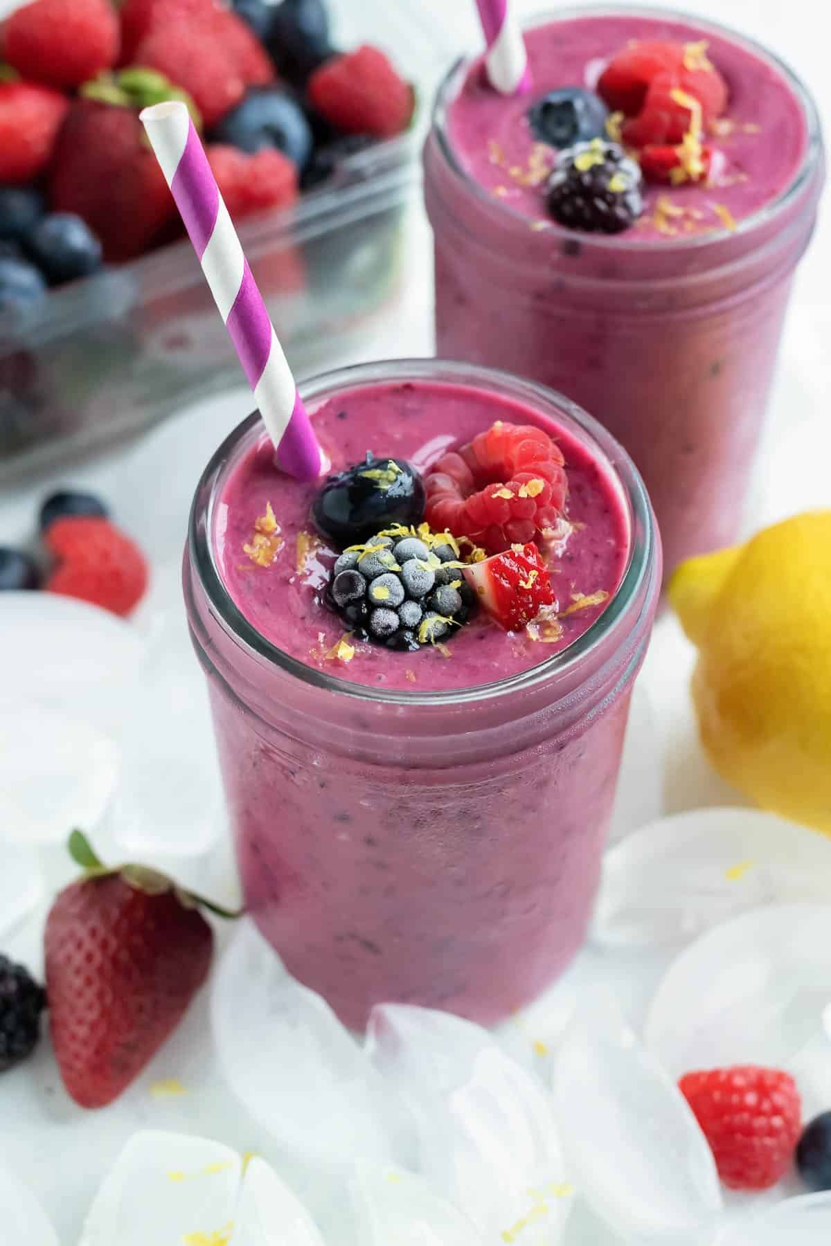 Healthy berry smoothies are served in glasses on the counter ice around them.
