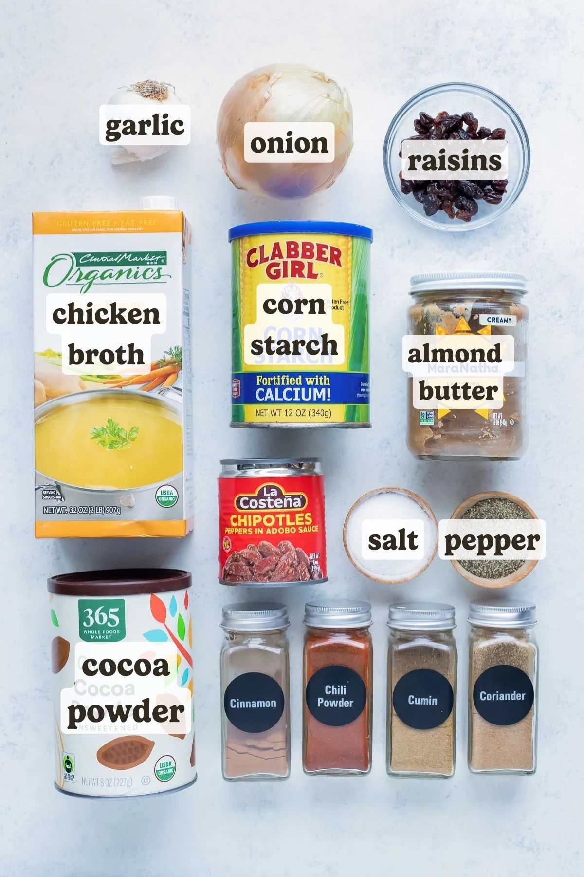 Cocoa powder, almond butter, chicken broth, raisins, and Mexican spices are on a counter as the ingredients for an easy mole sauce recipe.