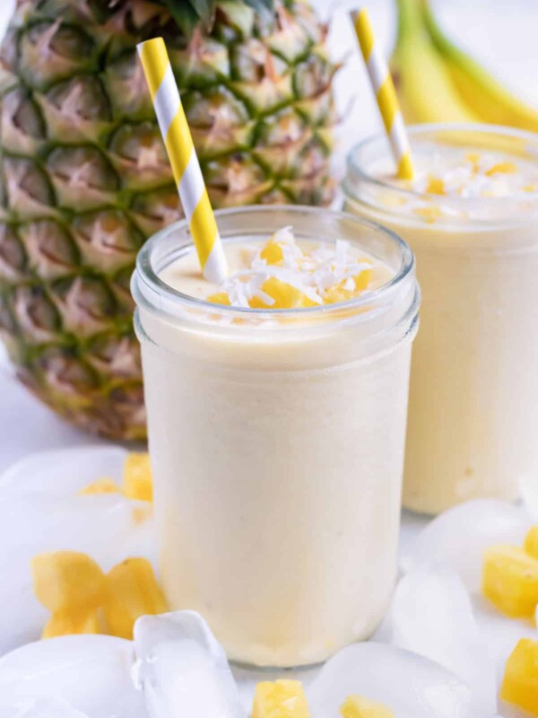 Two smoothies are set on the counter next to a fresh pineapple