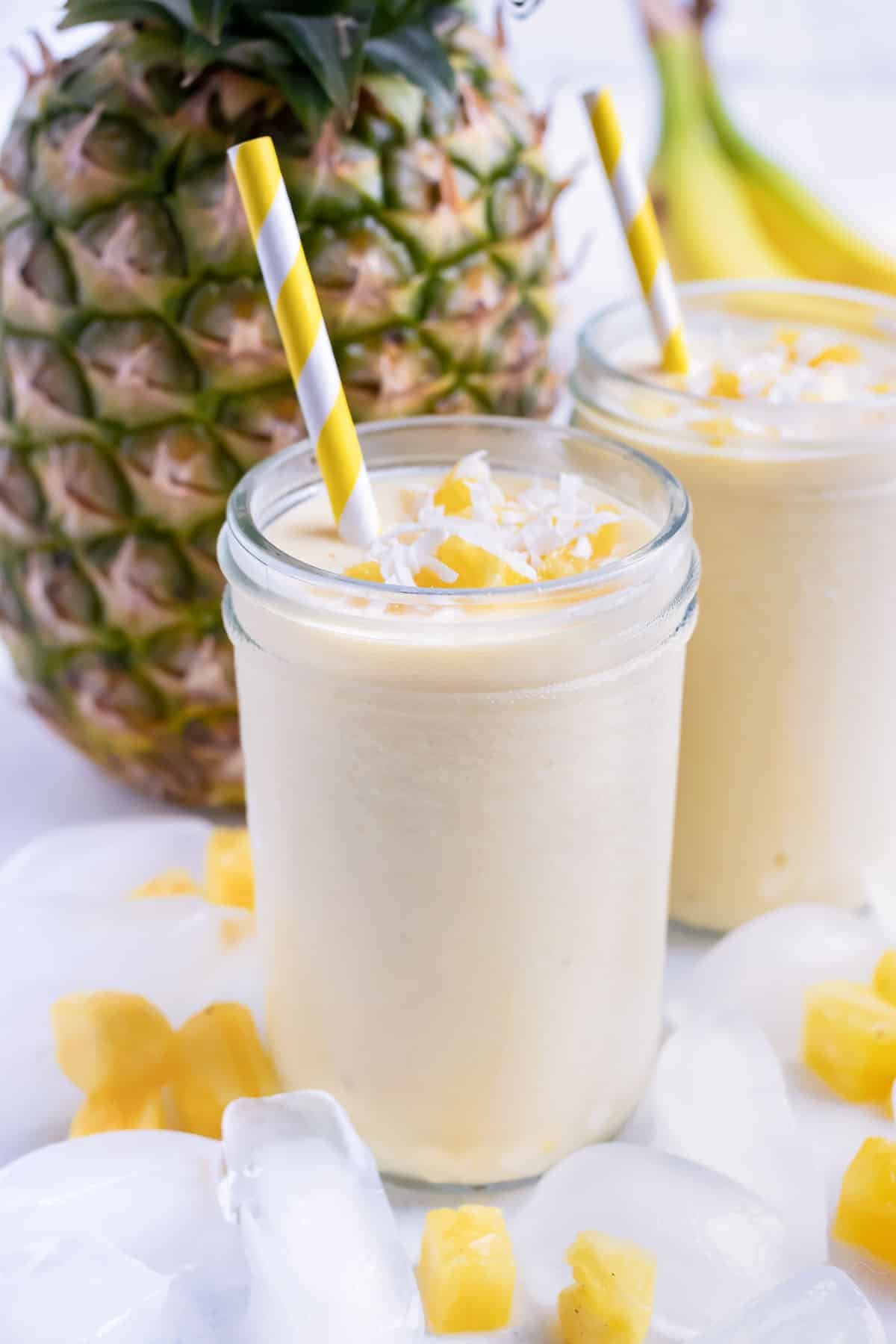 Two smoothies are set on the counter next to a fresh pineapple