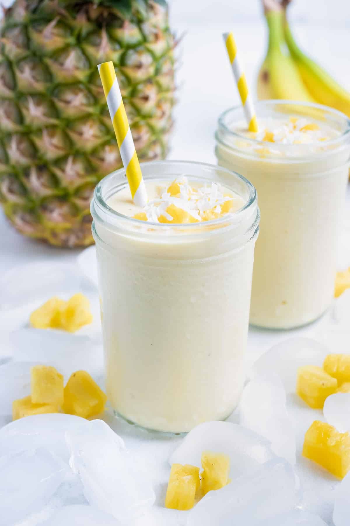 Two smoothies are set on the counter with pineapple and banana.