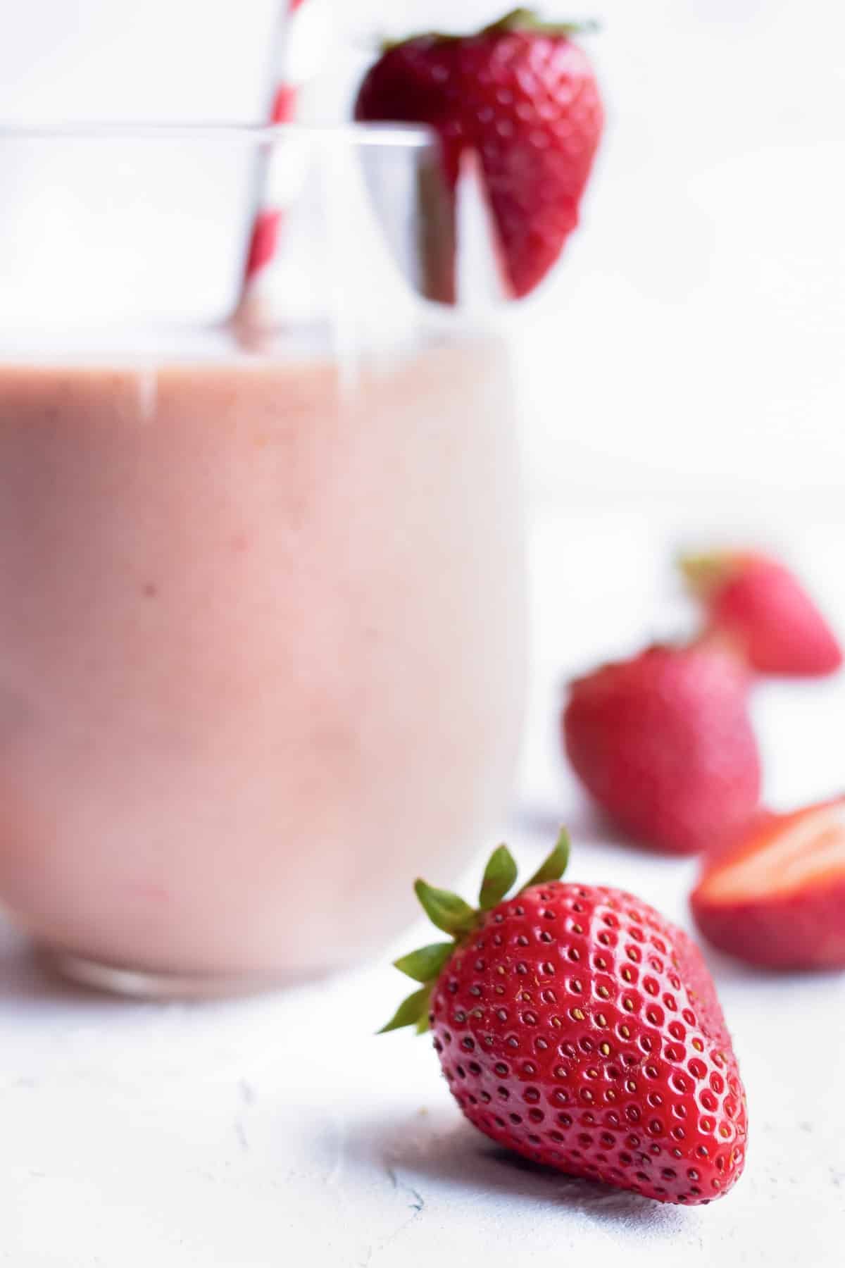 Fresh strawberries lying next to a glass full of a smoothie recipe.