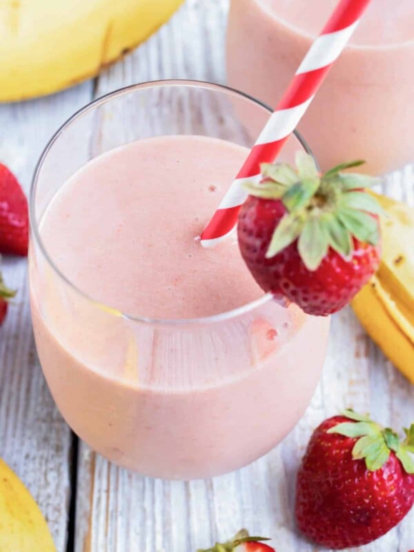 A glass full of a strawberry and banana smoothie with a strawberry as a garnish and a red/white striped straw.