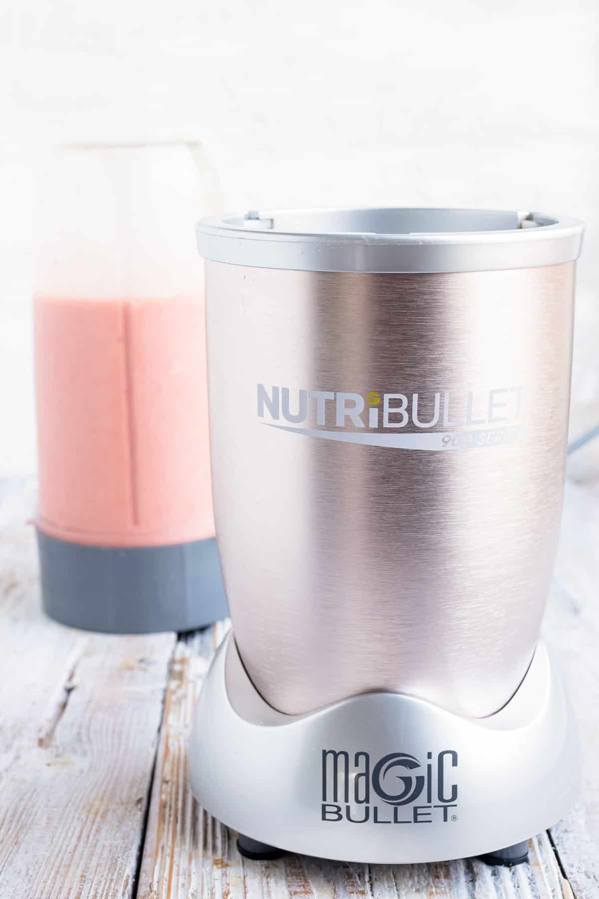 A Nutribullet, or high speed blender, with a strawberry smoothie in the background.