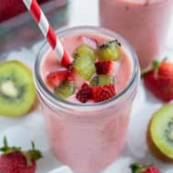 A creamy strawberry kiwi smoothie is topped with fresh kiwis and strawberries.