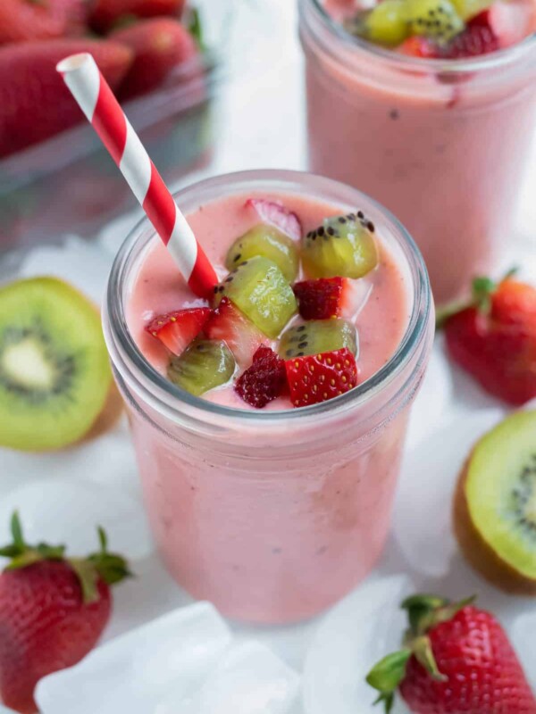 A creamy strawberry kiwi smoothie is topped with fresh kiwis and strawberries.