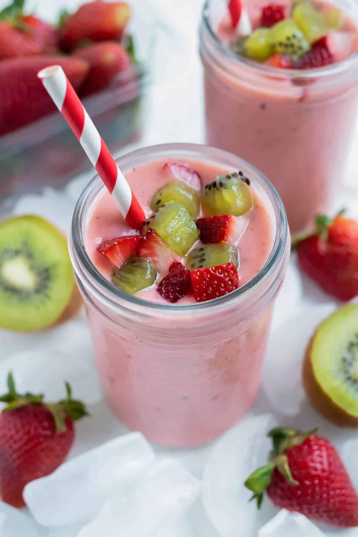 A creamy strawberry kiwi smoothie is topped with fresh kiwis and strawberries.