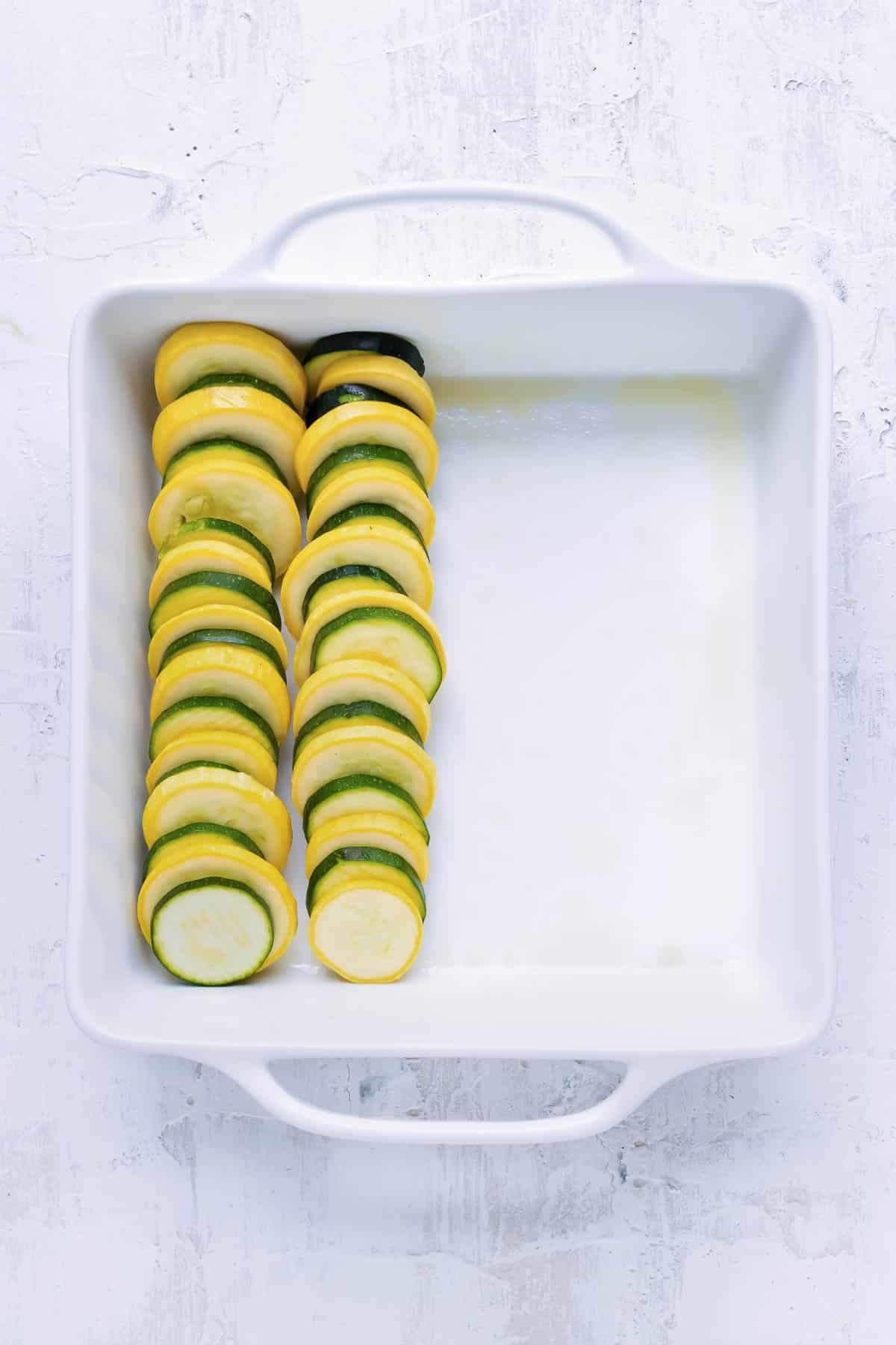 Yellow squash and zucchini are layered into a baking dish.