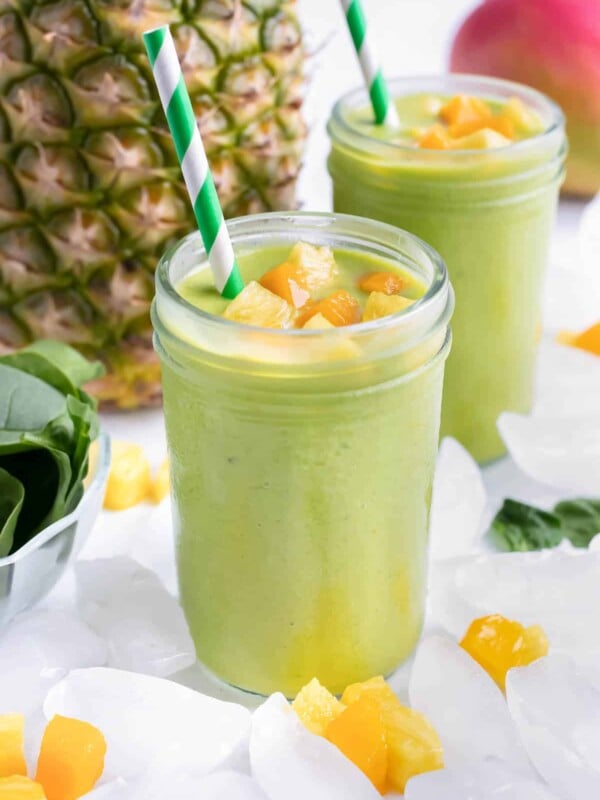 Two glasses are filled with a pineapple spinach smoothie.