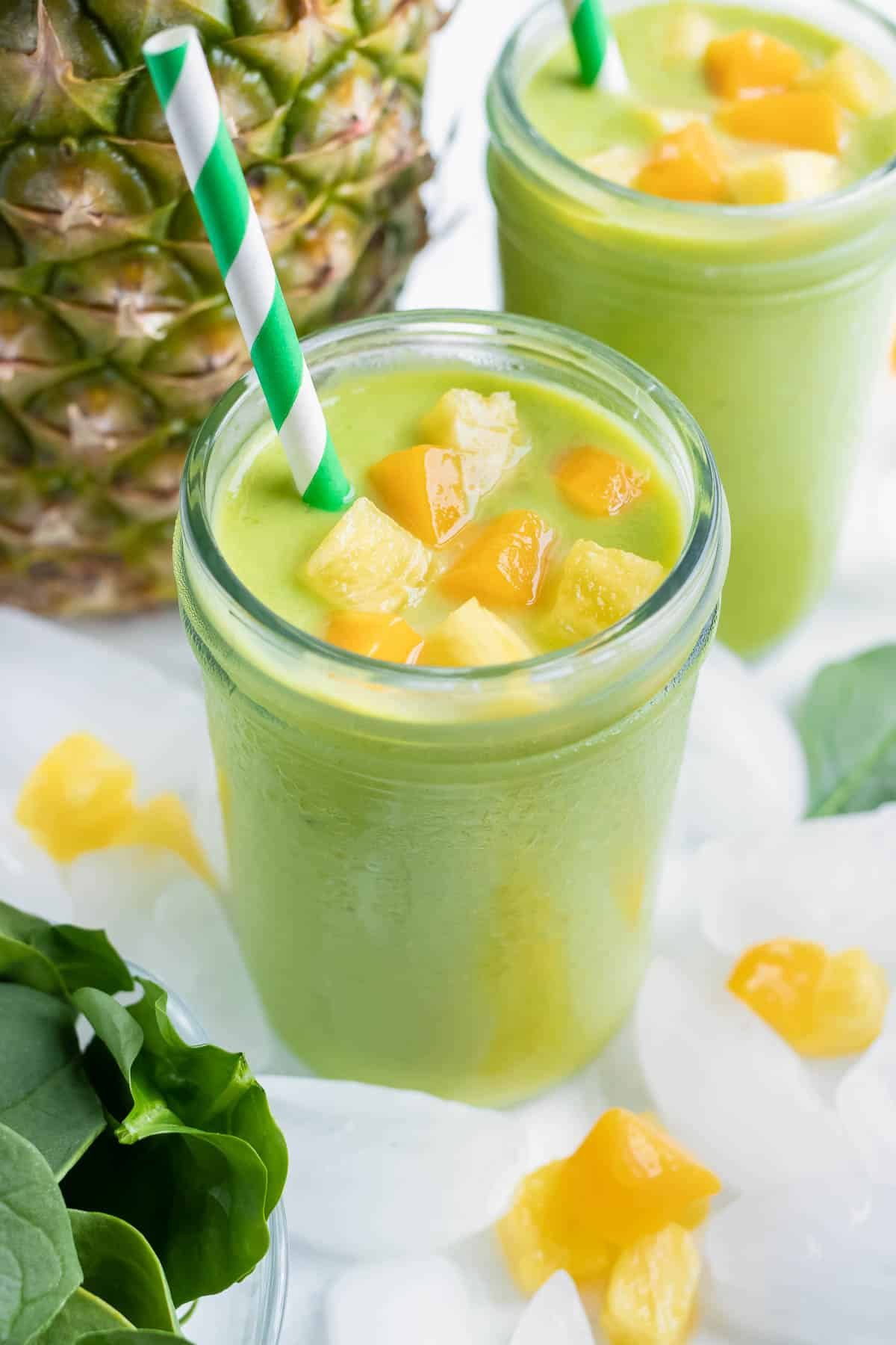 Two healthy green smoothies is set on the counter in a glass with a straw.