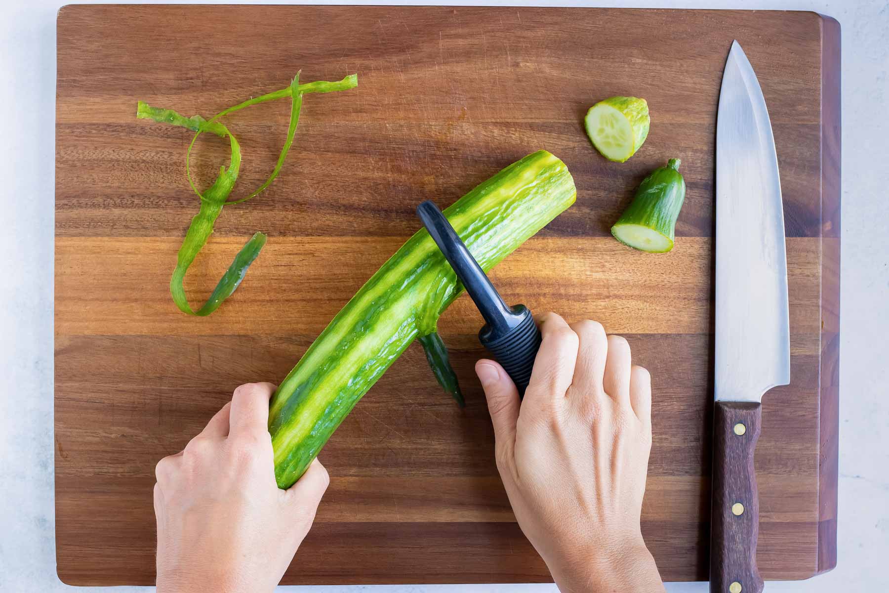 A cucumber is partially peeled before dicing.