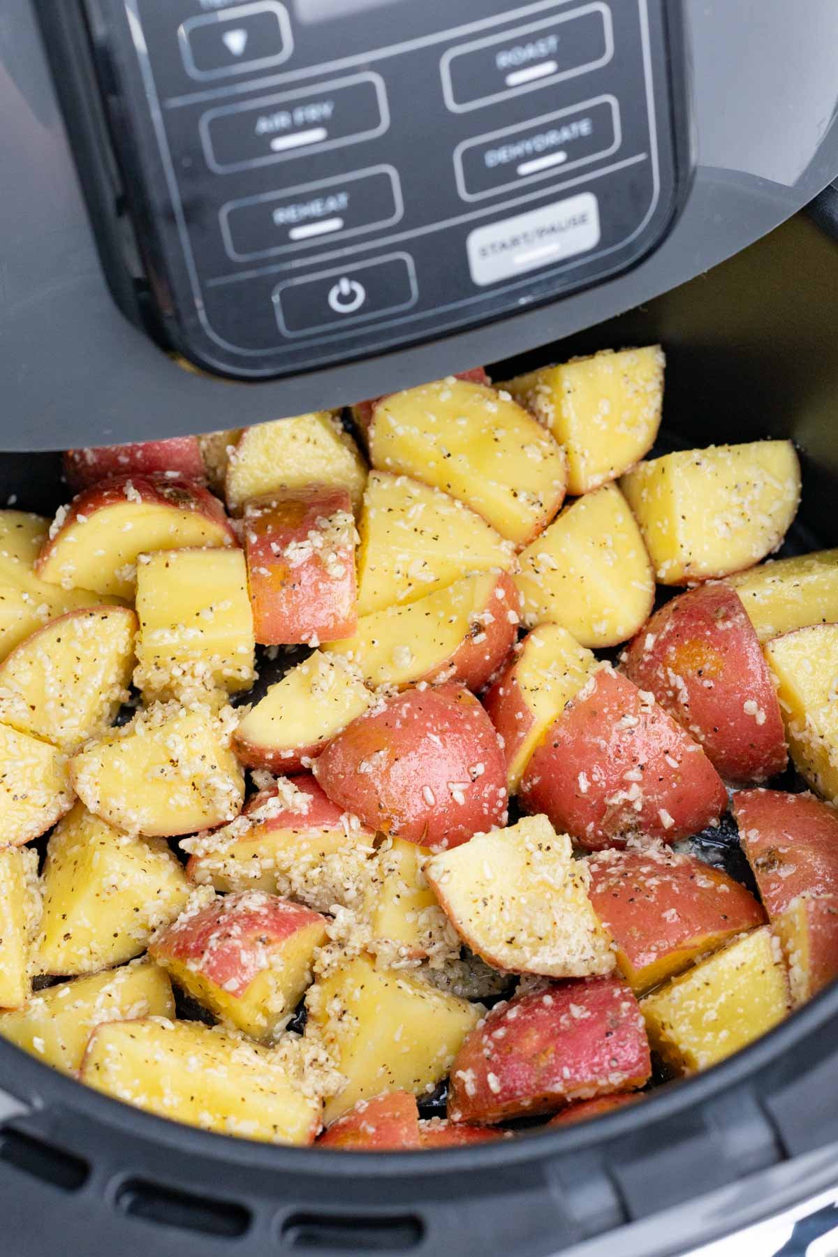 Seasoned potatoes with Parmesan are added to an air fryer.