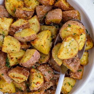 A spoon scoops out some air fryer roasted potatoes from a white bowl.