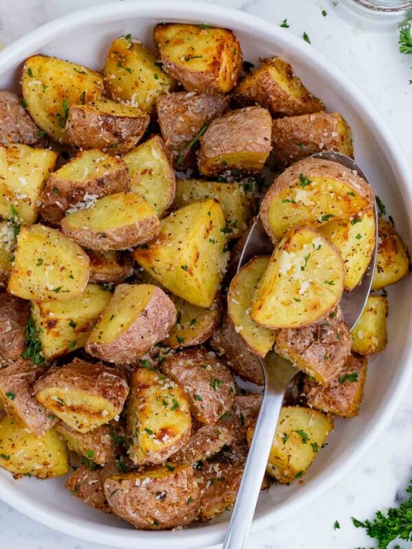 A spoon scoops out some air fryer roasted potatoes from a white bowl.