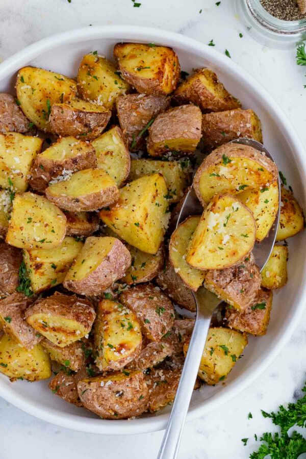 A spoon scoops out some air fryer roasted potatoes from a white bowl.