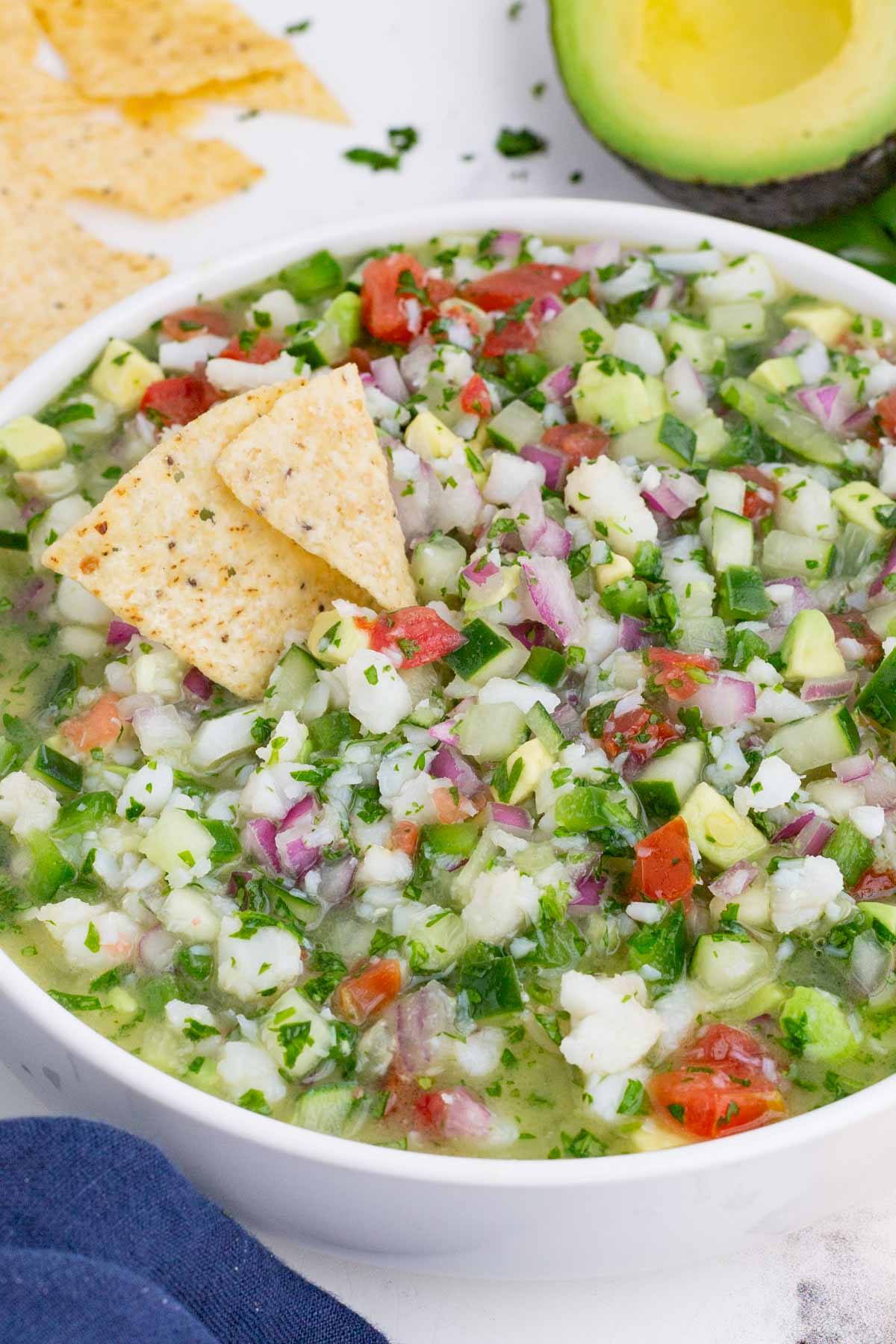 A Mexican dip made with bite-sized fish, avocado, cucumber, and tomato in a glass bowl.