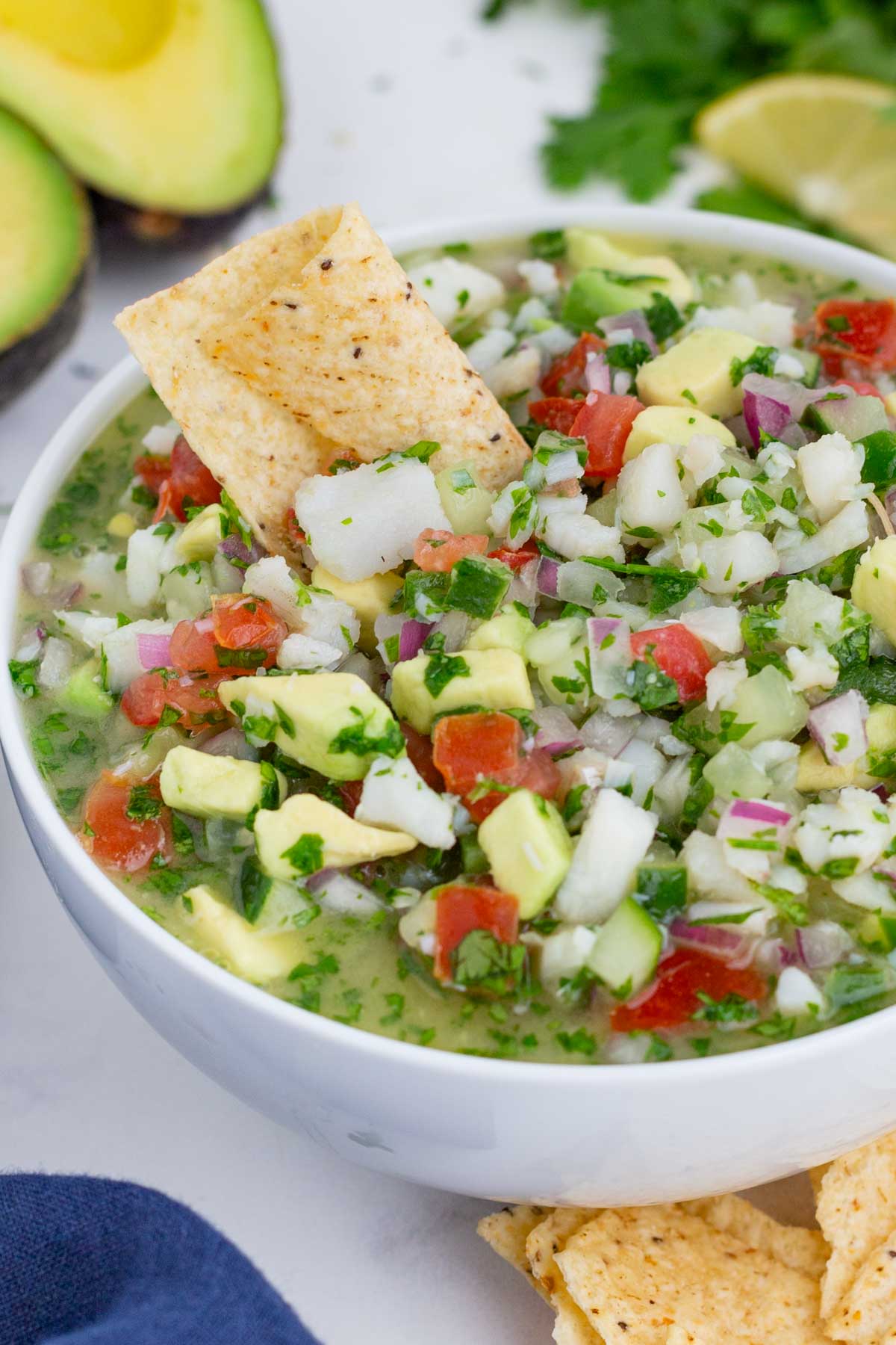 A Mexican dip made with bite-sized fish, avocado, cucumber, and tomato in a glass bowl.