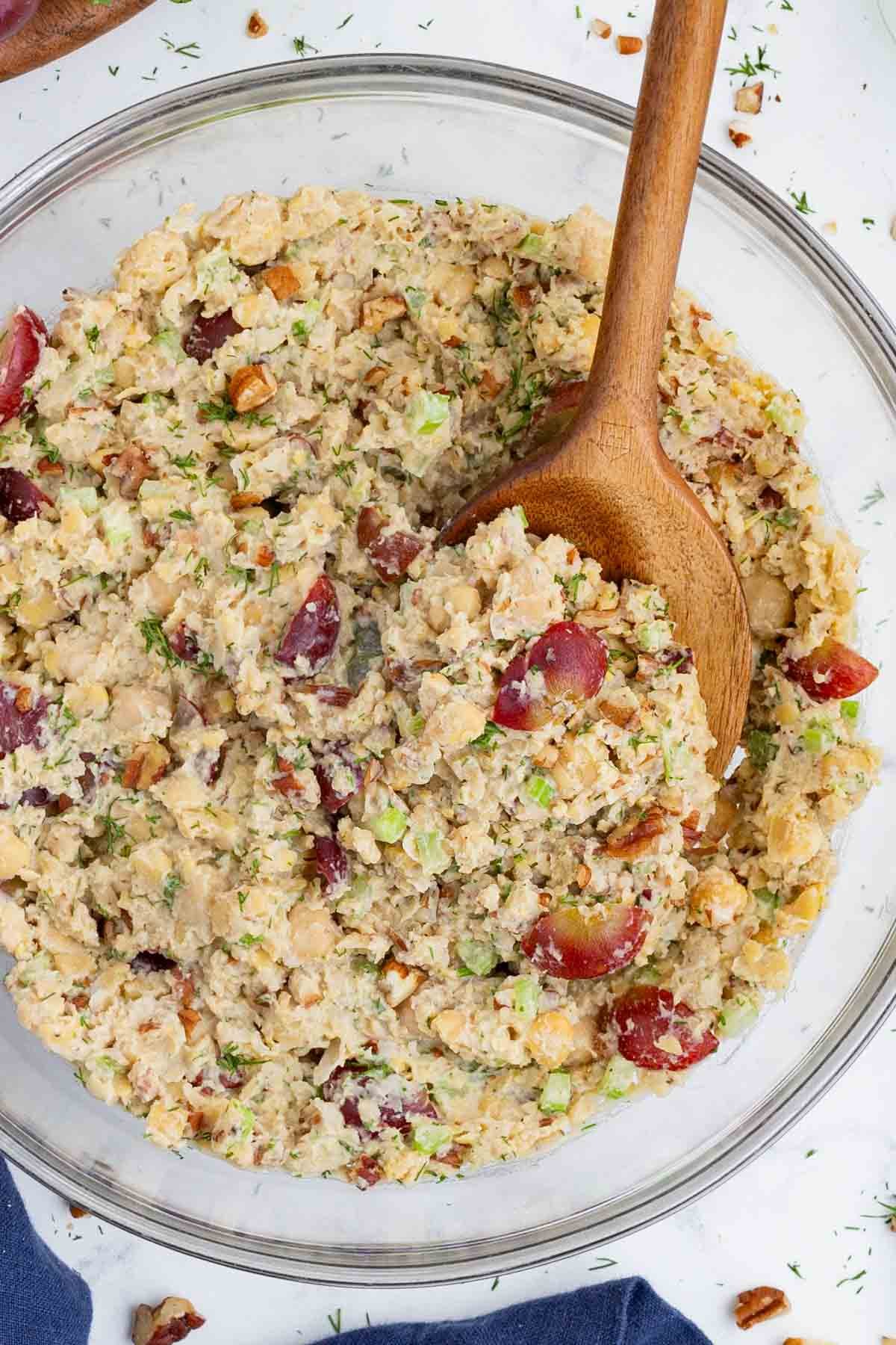 A wooden spoon stirs chickpea salad.