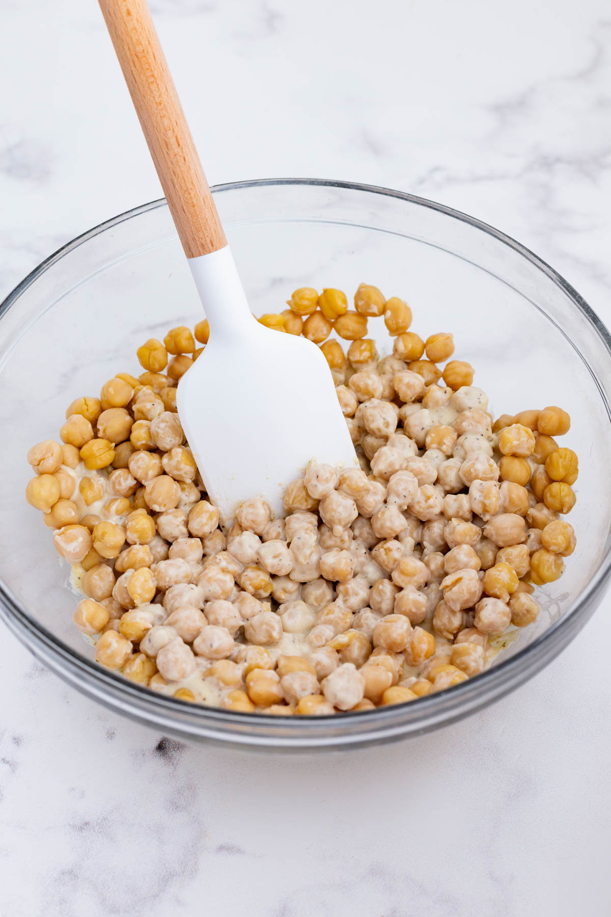 A spatula stirs the chickpeas into mayo mixture.