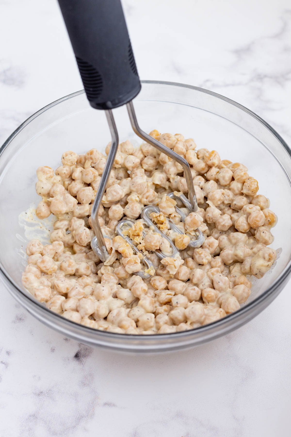 A potato masher smashes the chickpea salad mixture.