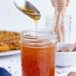 A spoon drizzles some hot honey over the jar.