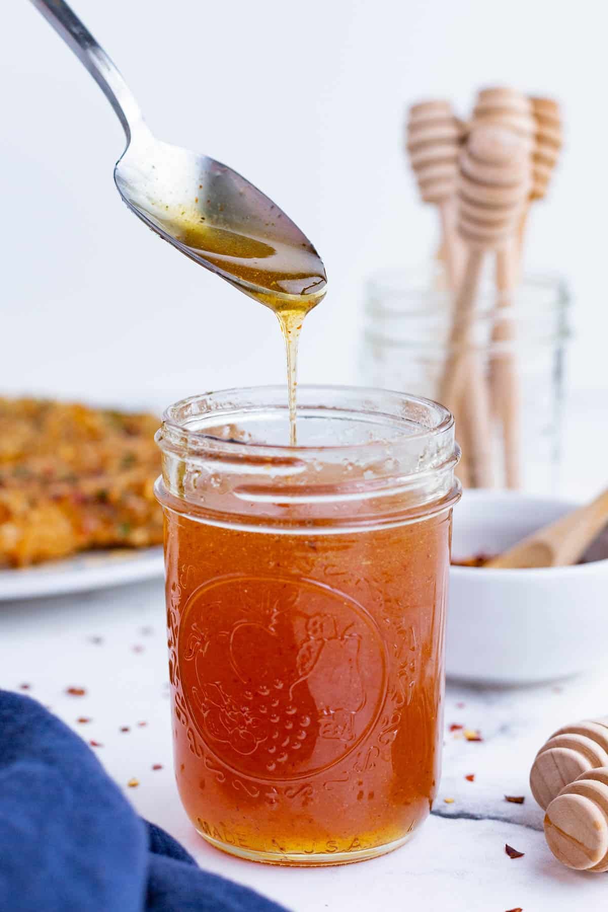 A spoon drizzles some hot honey over the jar.