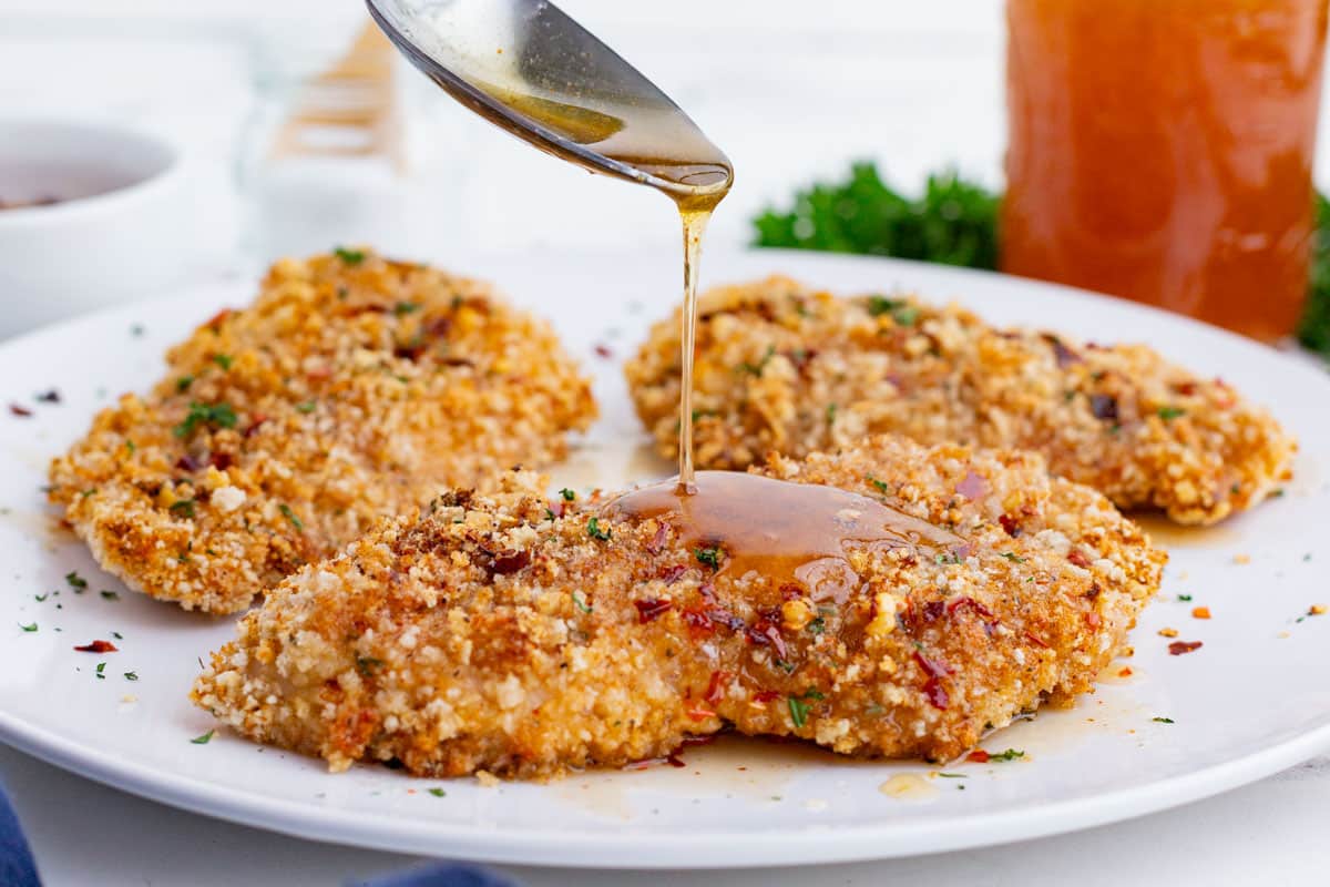 A spoon drizzles homemade hot honey over oven-fried chicken.