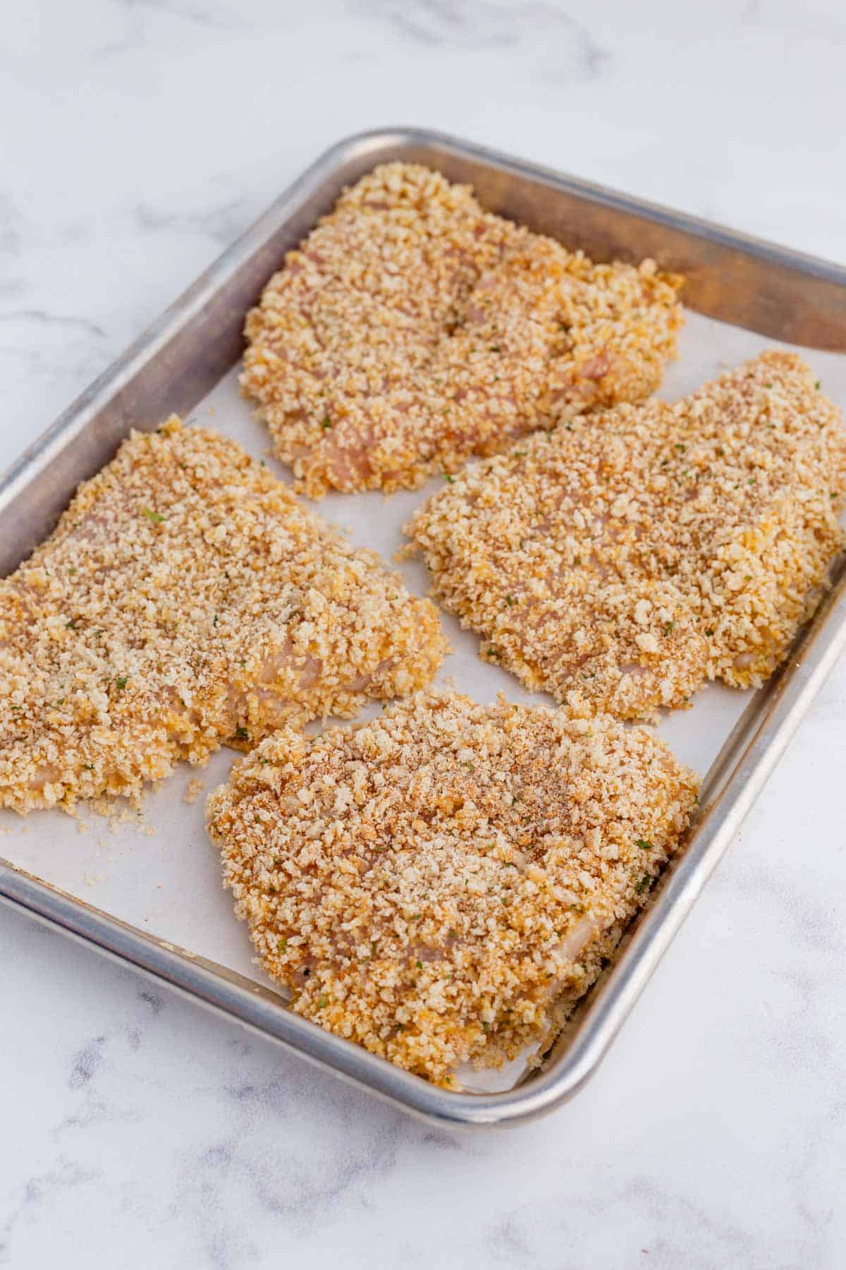 Breaded chicken is placed on a pan to bake.