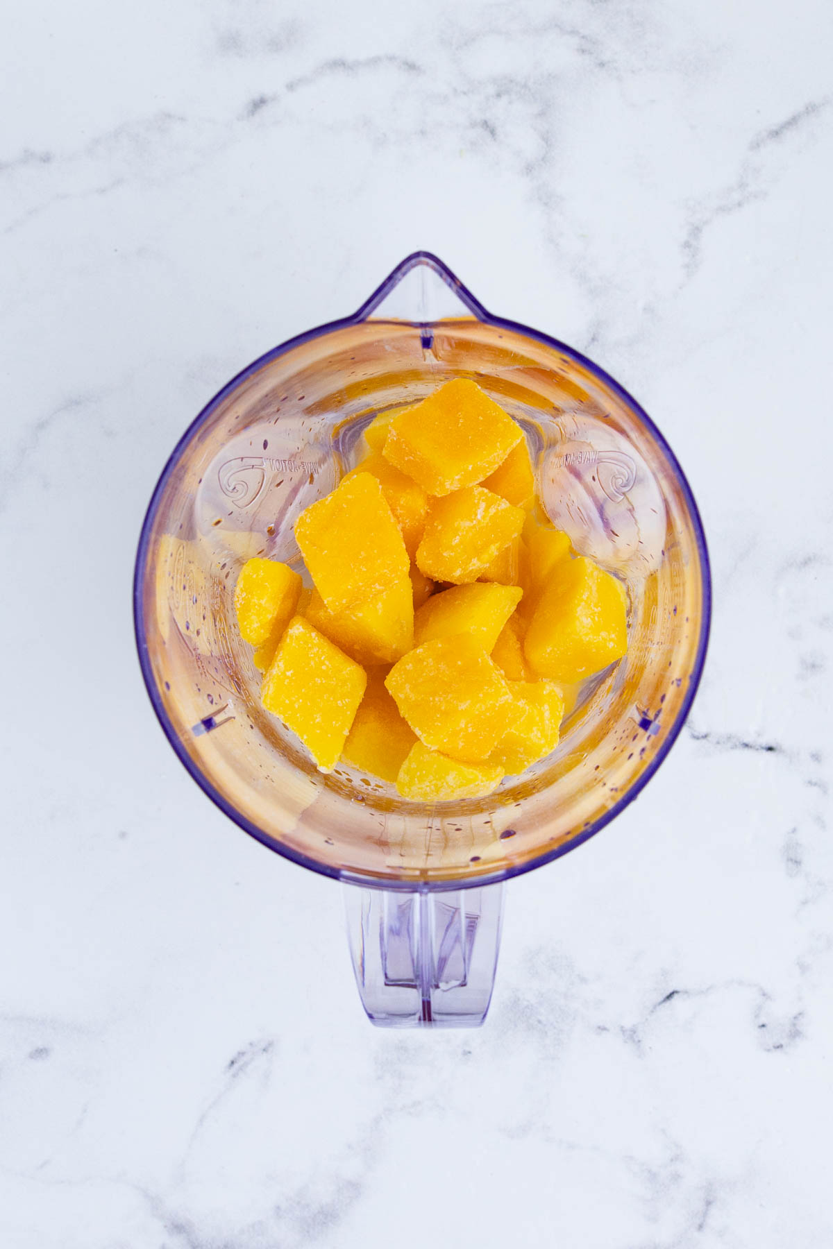 Frozen mango chunks and liquor are added to a blender.