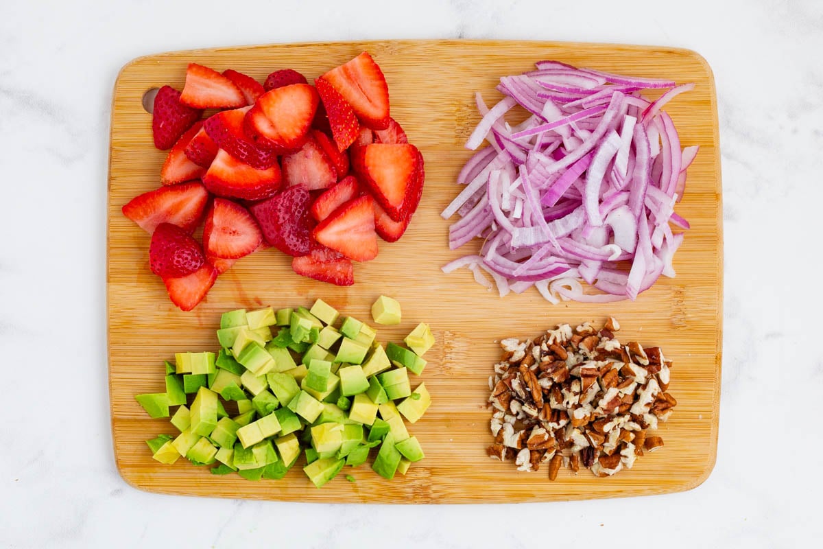 Strawberries, onion, avocado, and nuts are chopped.