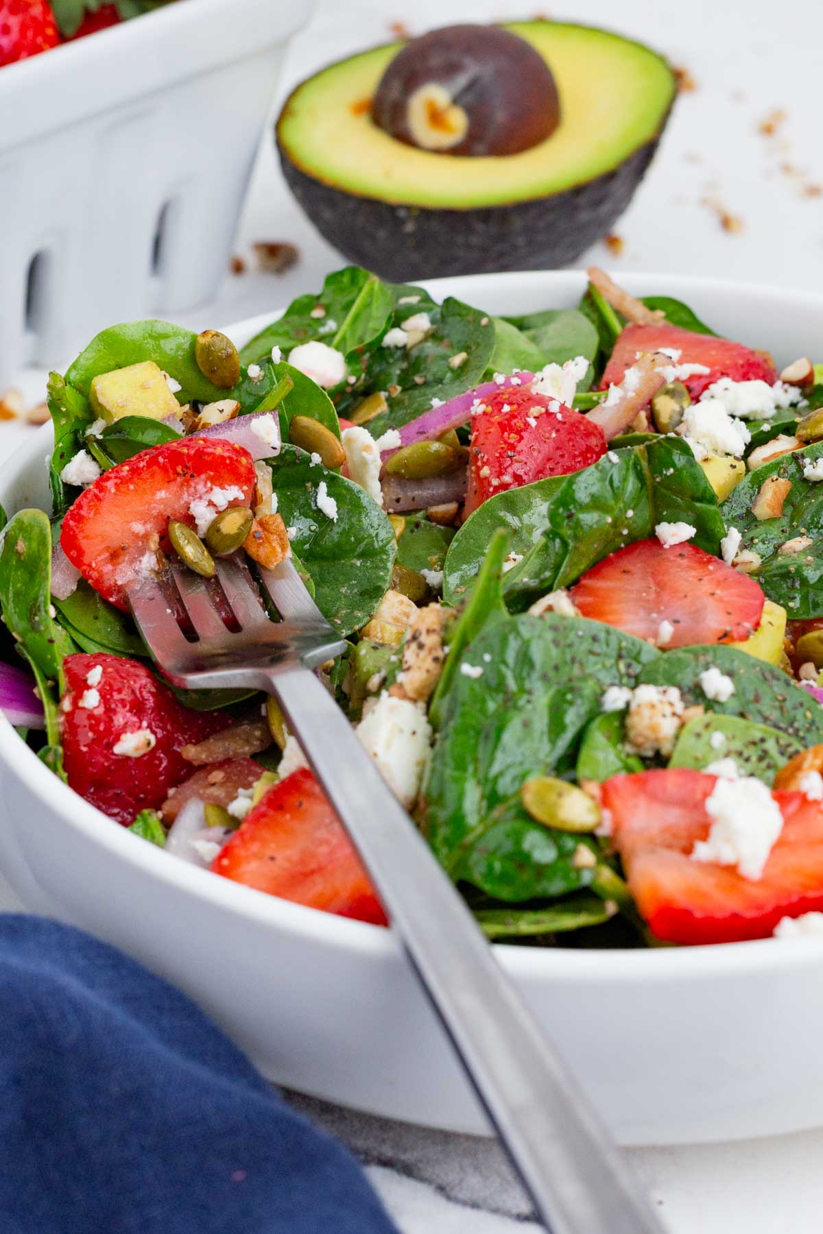 A fork rests on top of a bowl full of strawberry spinach salad with balsamic vinaigrette.