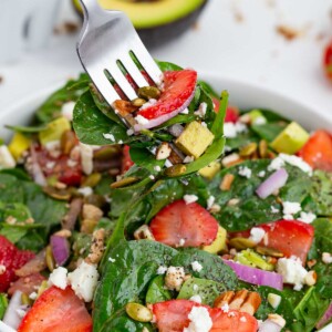 A fork scoops out a bite of this salad with spinach and strawberries.