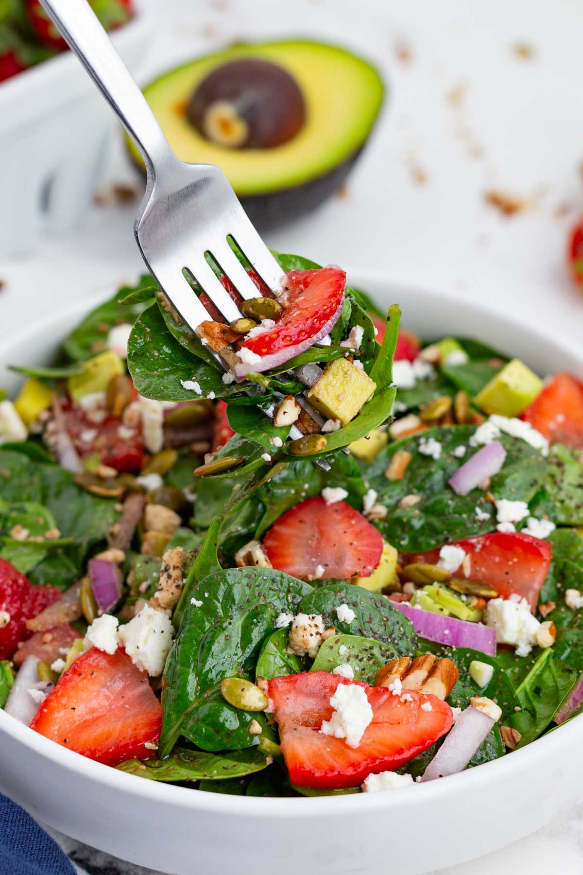 A fork scoops out a bite of this salad with spinach and strawberries.