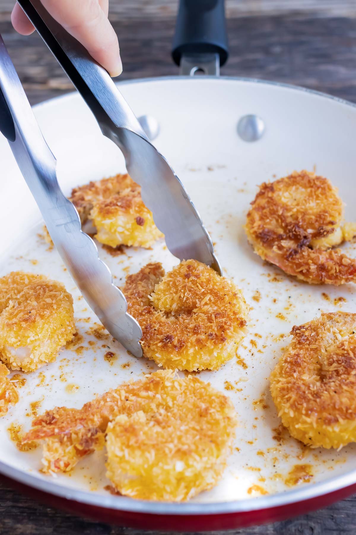 Tongs flips shrimp in a pan.