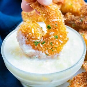 Fried coconut shrimp being dipped into a piña colada sauce.